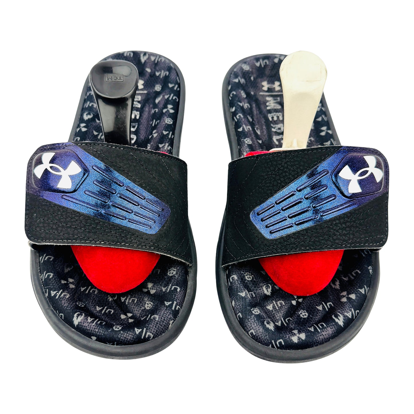 Pair of black Under Armour slides with red filling and Under Armour logo on a white background
