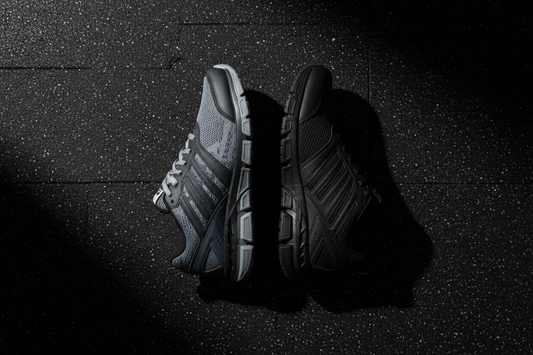 Under Armour and Adidas gym training shoes flat lay comparison on dark gym floor